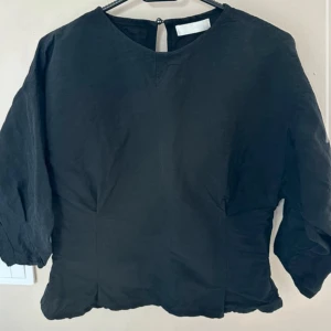 Svart långärmad tröja i bomull - En enkel svart långärmad tröja med rund hals. Tröjan är tillverkad i mjuk bomull och har en figursydd midja med trekvartsärmar. Perfekt för dig som gillar minimalistisk stil.