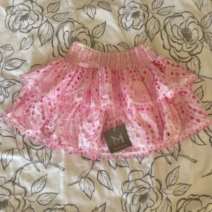 Rosa volangkjol från March Studio - Helt ny supersöt rosa kortkjol med volanger från March Studio. Kjolen har broderade spetsdetaljer och ett prickigt mönster, samt bred resår i midjan för skön passform. Perfekt för dig som gillar romantisk och lekfull stil.