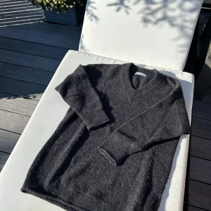 Mörkgrå stickad tröja Acne Studios - Säljer en mörkgrå stickad tröja från Acne Studios med v-ringad hals och långa ärmar. Tröjan har en mjuk och fluffig känsla, perfekt för kyliga dagar. 