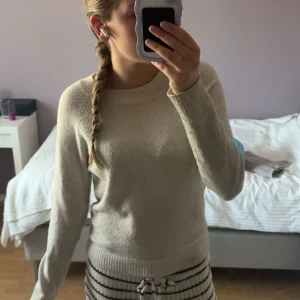 Beige stickad tröja med rund hals - Mysig beige stickad tröja med rundad hals och långa ärmar. Perfekt för kyliga dagar och enkel att matcha med olika outfits. Tröjan har en klassisk, normal passform och ribbade muddar vid ärmslut och nederkant.