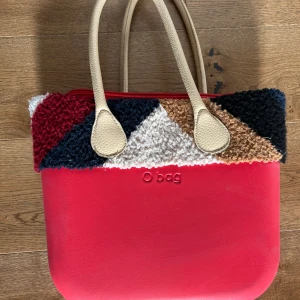 Röd O bag handväska med pälsdetalj - Supersnygg röd  oBag, ca 35cm bred 29cm hög.  Röd rymlig innerväska med ett lite bredare fack samt två mindre. Beige axelremmar i skinnimmitation, multifärgad ’fåll’ + en extra fåll att byta med i silver/grå lite ’fluffig’. Själva väskan är i något ’thermoplastic’ material så den är vattentät och lätt att göra ren. Sparsamt använd