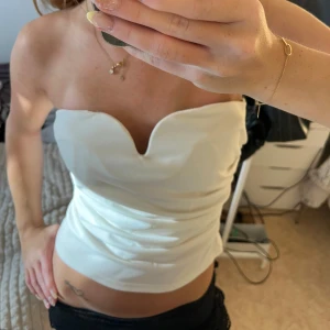 Vit axelbandslös tubtopp med sweetheart - Säljer en stilren vit tubtopp med snygg sweetheart-urringning. Toppen är axelbandslös och har en figurnära passform som framhäver siluetten. Perfekt för dig som vill ha en clean och chic look. Materialet känns slätt och har en lätt glans.