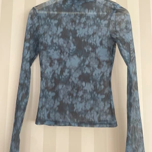 Blå mesh polotopp med mönster - Säljer en blå mesh top med lång ärm och coolt abstrakt mönster. Tunn och genomskinlig, perfekt att styla lager på lager. Slim fit och stretchigt material som sitter snyggt. Hög krage för extra edge.
