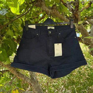 Mörkblå jeansshorts Forever 21 - Snygga mörkblå jeansshorts från Forever 21 med hög midja och klassisk femficksdesign. Shortsen har uppvikta ben, knapp och dragkedja framtill samt två bakfickor. Perfekta för varma dagar och enkel att matcha med din favorit-topp. Storlek 42. Helt ny med tags/ prislapp fortfarande kvar. 