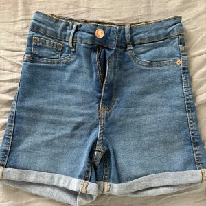 Blå jeansshorts från Gina Tricot - Snygga blå jeansshorts från Gina Tricot, modell Molly. De är högmidjade med klassisk femficksdesign, uppvikta benslut och gul kontrastsöm. Aldrig använda.