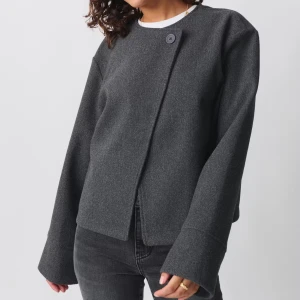 One-Button Jacka från GinaTricot  - Snygg grå jacka från GinaTricot med omlott-design och en stor knapp framtill. Jackan har en rak, croppad passform och långa ärmar med breda muddar. Perfekt för lite kyligare dagar. Använd endast en gång. Slutsåld på hemsidan. Skriv för egna bilder.