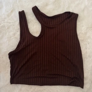 Brun ribbad linnetopp från Shein - Säljer en brun ribbad linnetopp från Shein i storlek XL. Toppen har ett asymmetriskt snitt med breda axelband och är tillverkad i mjuk polyester. Perfekt för dig som gillar en chill och trendig look med lite edge.