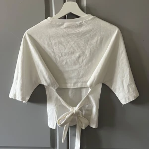 Open back tie tee från Nelly - Supersnygg vit croppad topp från Nelly med öppen rygg som man knyter i storlek xxs. Jag har endast använde den 1-2 gånger, dock så har den några trådar som sticker ut lite men det syns ingenting när man har på sig den.💕