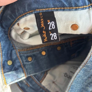 Nudie Jeans Grim Tim Workers Blue 28/28 - Säljer ett par Nudie Jeans Grim Tim i färgen Workers Blue. Klassiska blå jeans med raka ben, fem fickor och snygga kontrastsömmar. Materialet är 99% bomull och 1% elastan för lite stretch. Perfekta för dig som gillar en tidlös och clean look.