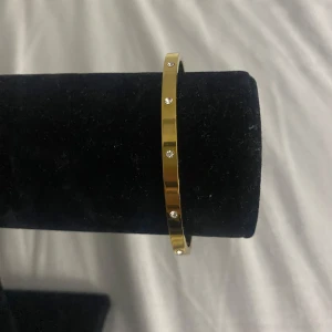 Guldigt armband med stenar - Snyggt och stilrent armband i guldton med små glittrande stenar runt om. Armbandet är smalt och har en rund form som ger en elegant vibe. Perfekt för dig som gillar minimalistiska smycken med lite extra bling. Helt oanvänd, fått i present. Tveka inte att höra av dig🌸