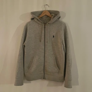 Grå ziphoodie från Ralph Lauren - Säljer en stilren grå ziphoodie från Ralph Lauren. Tröjan har en klassisk dragkedja och två fickor framtill. Tröjan fungerar både till lite avslappnad stil men också till mer finare tillfällen. I använt skick men ej några defekter👍🏻
