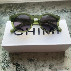Gröna solglasögon från CHIMI #003 - Snygga gröna solglasögon från CHIMI med rund form och mörka linser. Perfekta för att ge en cool touch till din stil. Ramen är transparent grön och har en modern design. Färgen är ”kiwi”