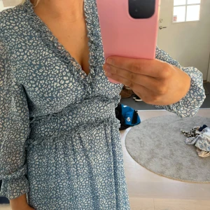 Blå klänning med mönster - Säljer en söt blå klänning med vitt mönster och volangdetaljer. Klänningen har trekvartsärmar och en v-ringad hals. Perfekt för en somrig look! Klänningen köptes på plick därav vet jag inte vart den är ifrån men den är i nytt skick. Skriv för fler bilder eller frågor ❤️