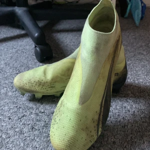 Gula fotbollsskor från Puma - Säljer ett par gula fotbollsskor från Puma med svarta detaljer. Skorna har en strömlinjeformad design utan snörning och är perfekta för snabba rörelser på planen. De har dobbar för bra grepp på gräs.