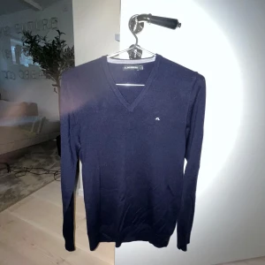 Mörkblå tröja från J.Lindeberg - Snygg mörkblå tröja från J.Lindeberg med v-ringning och diskret logga på bröstet. Perfekt för en stilren look. Använd ca 5 gånger och tvättad två gånger, inga defekter. Nypris: 1500k
