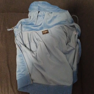 Blå velourjacka från Juicy Couture - Säljer en snygg blå velourjacka från Juicy Couture. Jackan har en dragkedja framtill och en mysig huva med snörning. Perfekt för en avslappnad stil. 💙