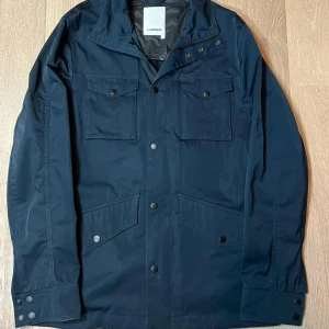  J.Lindeberg vårjacka - Snygg svart jacka från J.Lindeberg med knappar och dragkedja. Jackan har flera fickor med knappstängning och en stilren design. Perfekt för en modern look. Priset går att diskuteras!