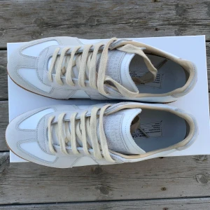 Vita Gats från Maison Margiela - Snygga vita sneakers från Maison Margiela med beige mockadetaljer och gummisula. Skorna har klassisk snörning och en stilren design som passar perfekt för en avslappnad look.