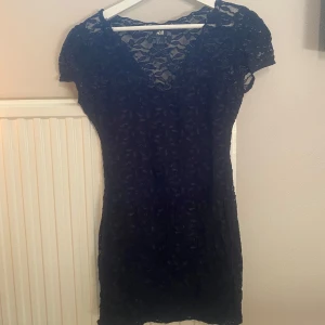 Svart spetsklänning från H&M - Snygg svart klänning från H&M med spetsdetaljer och korta ärmar. Klänningen har en v-ringad design som ger en relaxed fit.