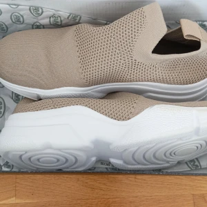 Beige sneakers från 157 - Säljer ett par beige sneakers från 157 med en stickad ovandel och vit sula. Skorna har en slip-on design utan snörning, vilket gör dem enkla att ta på och av. Perfekta för en avslappnad stil. Finns några fläckor men går att ta bort säkert.