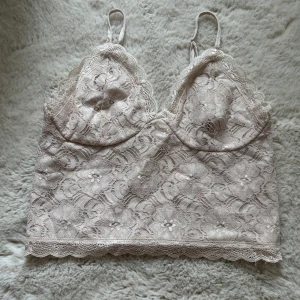 Beige crop top - Säljer ett vackert beige spetslinne med justerbara axelband. Toppen har ett blommigt spetsmönster och en elastisk rygg för extra komfort.