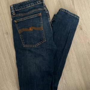 Blå slim jeans från Nudie - Snygga blå slim jeans från Nudie med klassisk femficksdesign och knappgylf. Perfekta för en stilren look. Tillverkade i en stretchig denim för extra komfort. Skinny lin heter modellen