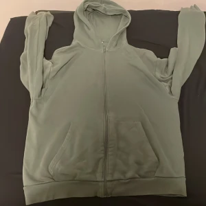 Grön hoodie från H&M - Säljer en grön hoodie från H&M med dragkedja och fickor framtill. Perfekt för en avslappnad stil. Den har långa ärmar och en mjuk känsla.