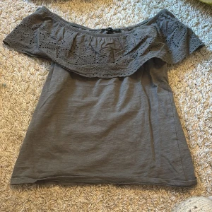 Grå offshoulder topp med spetsdetaljer - Säljer en stilren grå offshoulder topp med vackra spetsdetaljer runt axlarna. 