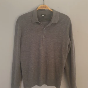 Grå långärmad polotröja från Uniqlo - Säljer en stilren grå långärmad polotröja från Uniqlo. Tröjan har en klassisk krage med knappar och är tillverkad i ett mjukt material som passar perfekt för kyligare dagar. Perfekt för en avslappnad men ändå snygg look.