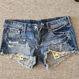Blå jeansshorts - Snygga blå jeansshorts med slitna detaljer och fransar. Shortsen har en låg midja och leopardmönstrade fickor som ger en cool touch. Perfekta för en avslappnad stil.