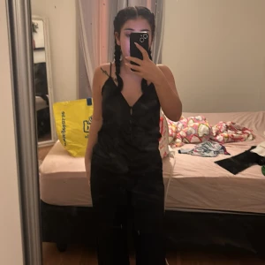 Svart satinlinne - Säljer ett elegant svart linne i satin med smala axelband och djup rygg. Perfekt för en stilren look.