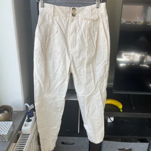 Vita byxor med knappar - Snygga vita byxor med hög midja och två dekorativa knappar framtill. Byxorna har en loose passform. Bomull.