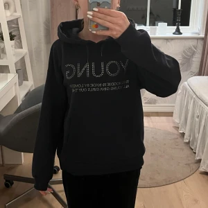 Mörkblå  hoodie från Gina Tricot - Säljer en mörkblå hoodie från Gina Tricot med texten 'YOUNG' i glittriga stenar plus lite mer text på framsidan. Tröjan har en stor ficka framtill och en bekväm huva. Perfekt för en avslappnad stil. Använt typ 2 gånger. Den är som ny! Den kostade 300 kr när jag köpte den. Den är super fin och jätte skön! Den är även mjuk på insidan vilket gör den ännu gosigare! 😍