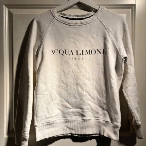 Vit sweatshirt från Acqua Limone - Säljer en vit sweatshirt från Acqua Limone med tryck fram och en stor gul citron på baksidan. Tröjan har långa ärmar och ribbade muddar vid ärmslut och nederkant. Perfekt för en avslappnad stil!