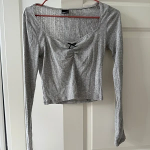 Grå ribbad topp från Gina Tricot - Säljer en stilren grå ribbad topp från Gina Tricot. Toppen har långa ärmar och en söt liten rosett framtill. 