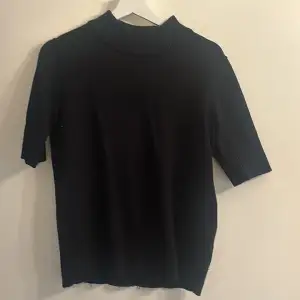 Säljer en stilren svart tröja från Vila med korta ärmar och hög krage. Perfekt för en minimalistisk look. Tröjan är tillverkad i ett mjukt material som ger en bekväm passform.