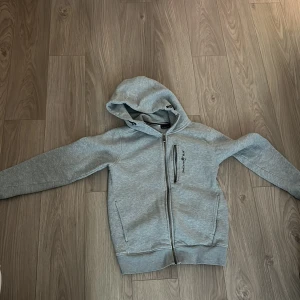 Grå hoodie från Sail Racing - Säljer en grå sailracing tröja då de inte är min stul längre. Dragkedjan har tappat lite färg men inte mycke för att vara köpt för ett år sedan. Den är rätt så använd men inga fläckar eller några sorts skador.