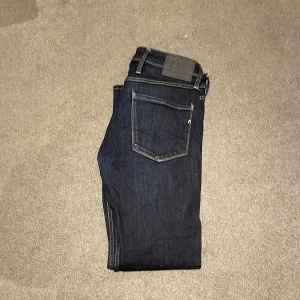 Mörkblå jeans från Replay - Snygga mörkblå jeans från Replay med klassisk fickdesign och kontrastsömmar. Byxorna har en knappgylf och bälteshällor, vilket gör dem perfekta för en avslappnad stil. Märkeslogga på bakfickan ger en extra touch. Pris kan diskuteras