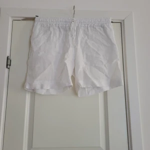 Vita linne shorts - Säljer ett par vita shorts i linne med elastisk midja och snörning. Perfekta för varma sommardagar med sin lätta och luftiga känsla. De har en avslappnad passform som gör dem bekväma att bära hela dagen.