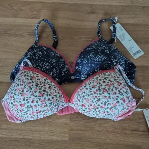 Två-pack mönstrade BH:ar 70AA helt nya - Säljer ett set med två BH:ar från Esprit. Den ena är vit med blommigt mönster i rosa och grönt samt randiga detaljer. Den andra är mörkblå med ett vitt blommönster. Båda har justerbara axelband och spetsdetaljer. Storleken är 70AA på båda. Bägge är helt oanvända med orginaletiketten kvar. Kom med prisförslag.