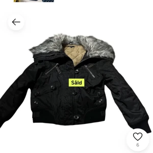 Svart jacka med pälsdetaljer - Snygg svart jacka med päls på huvan och dragkedja framtill. Vintage y2k jacka från Kappahl. Jackan har knappar och ribbade muddar vid ärmslut och nederkant. Perfekt för kyligare dagar.