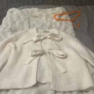 Vit stickad kofta från Gina Tricot - Säljer en superfin vit stickad kofta från Gina Tricot i premiumkvalitet. Koftan har långa ärmar och två söta knytband framtill. Perfekt för att hålla sig varm och stilren under kyliga dagar. Säljer denna för att kunna köpa ett par jeans