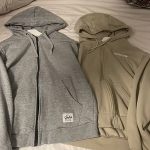 Grå och beige hoodies från Andy och McKenzie - Två snygga hoodies till salu! En grå hoodie från Andy i storlek M med dragkedja och vit insida. Den andra är en beige hoodie från McKenzie i storlek L. Båda har huva och fickor framtill. Perfekta för en avslappnad stil!