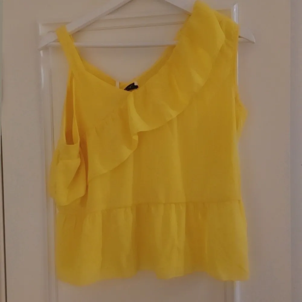 Säljer en solgul oneshoulder topp från Boohoo med volangdetaljer. Perfekt för sommardagar och ger en härlig färgklick till garderoben. Toppen har en luftig passform och är tillverkad i ett lätt material.Liten i storlek, mera som S/M I storleken . Yläosat.