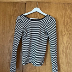 Svartvit randig topp - Säljer en stilren svartvit randig topp med långa ärmar. Toppen har en djup v-ringning och är perfekt för en avslappnad look. Den är gjord i ett mjukt och bekvämt material.