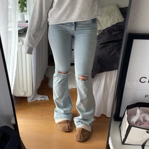Bootcut jeans med slitningar från Nelly - Ljusblå bootcut jeans från Nelly med låg midja och slitna hål över knäna. Snygga röda detaljer på bakfickorna och klassisk femficksmodell. Jeansen är i bomull och har en riktigt chill vibe med sin ljusa tvätt och slitna look.