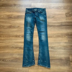 Hysteric Glamour Bootcut Jeans - Snygga blå bootcut jeans från Hysteric Glamour med slitna detaljer och coola nitar vid fickan. Jeansen har låg midja och klassisk femficksdesign. Perfekta för dig som gillar en edgy och unik stil. längd 106 midja 39