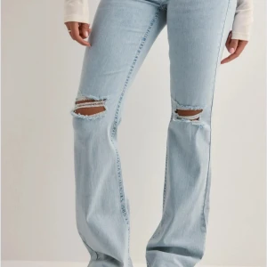 Lowwaist Bootcut ljusblå jeans med slitningar - Snygga ljusblå bootcut jeans med slitna hål på knäna och broderade detaljer på bakfickorna.