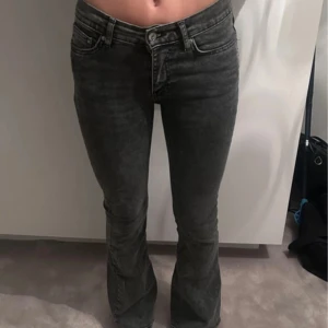 Gråa bootcut jeans med hög midja - Säljer ett par gråa jeans med bootcut-modell och hög midja. Jeansen har klassisk femficksdesign, dragkedja och knapp framtill. Materialet är denim med en snygg tvättad look. Perfekta för dig som gillar en trendig och bekväm stil.
