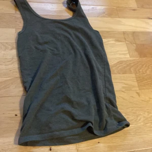 Mörkgrå linnetopp från FSBN Sister - En enkel och stilren mörkgrå linnetopp från FSBN Sister i storlek XXS. Toppen är ärmlös med klassisk rund halsringning och tillverkad i mjukt bomullsmaterial. Perfekt att matcha med jeans eller shorts för en avslappnad look.